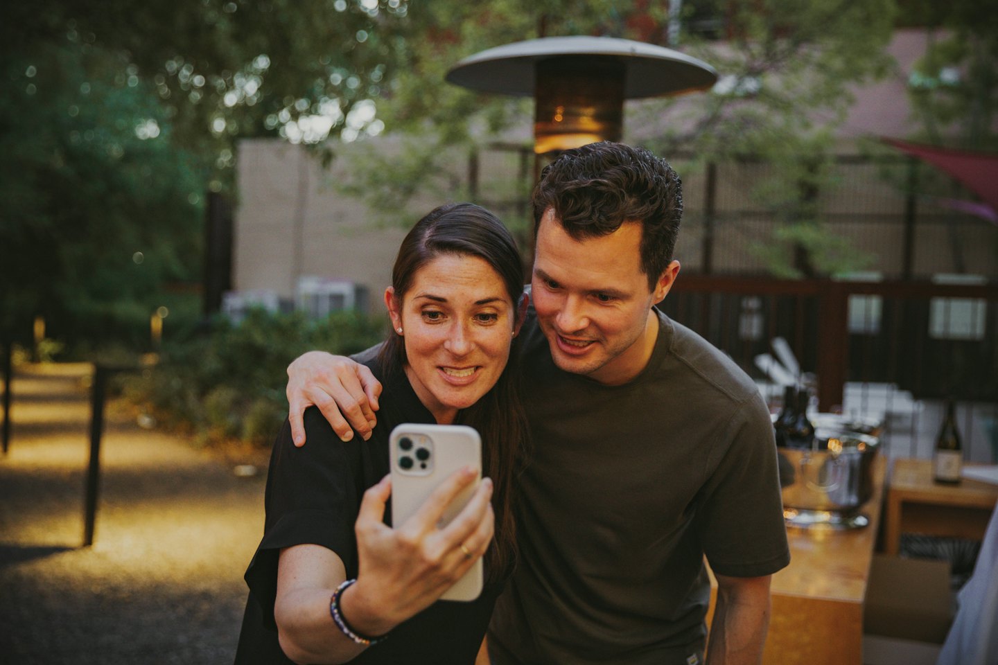 Couple smiling while looking at a smartphone together outdoors.